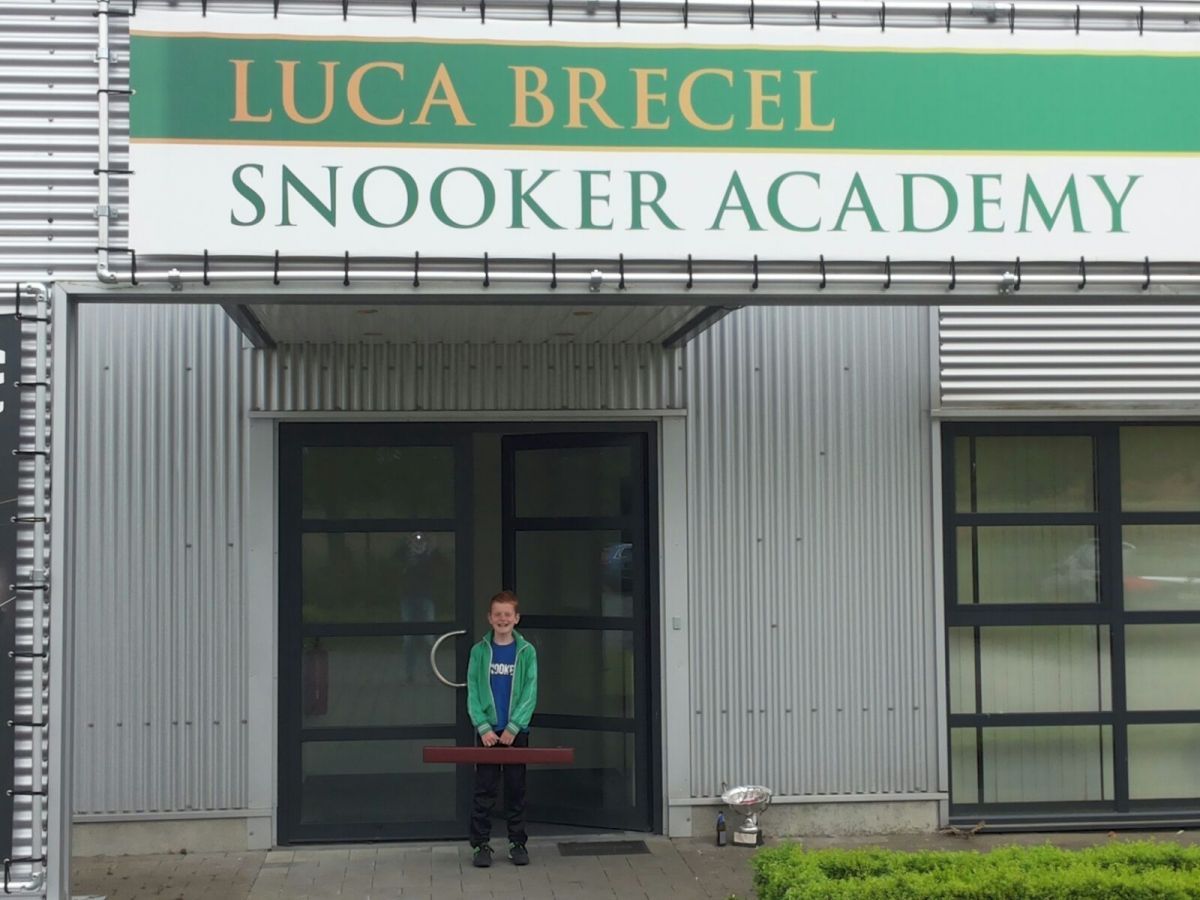 Een jongen staat bij de ingang van de Luca Brecel Snooker Academy.