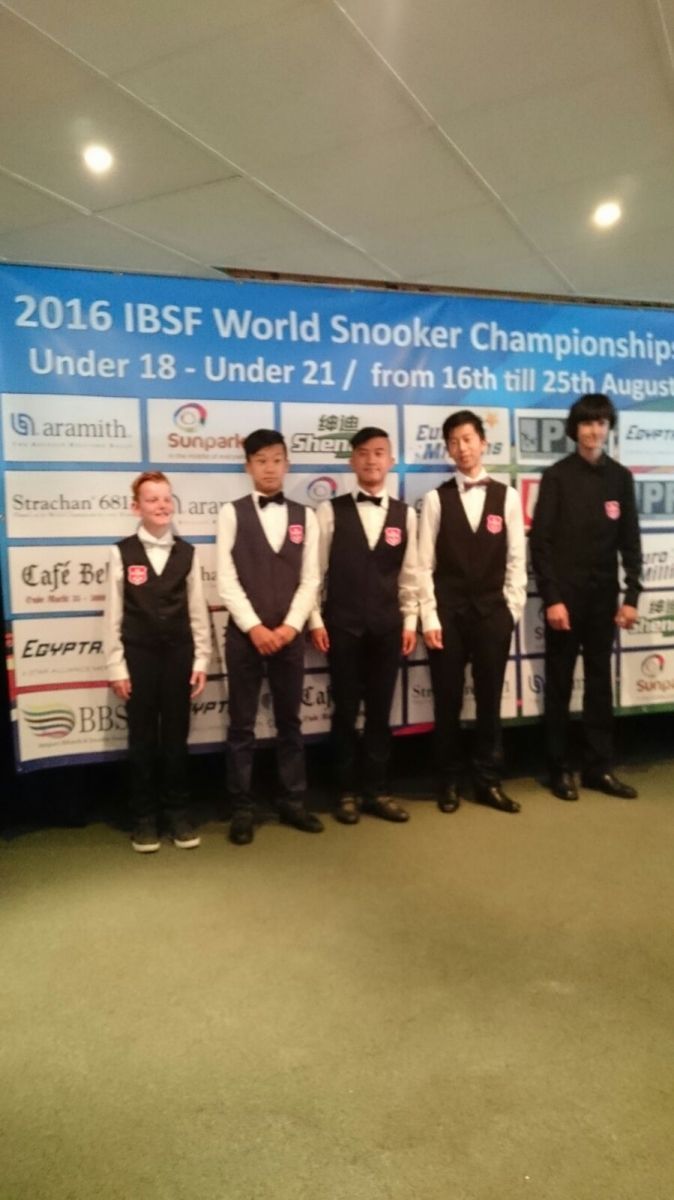 Vijf jonge snookerspelers in pakken staan ​​voor een spandoek ter ere van het IBSF Wereldkampioenschap Snooker van 2016.
