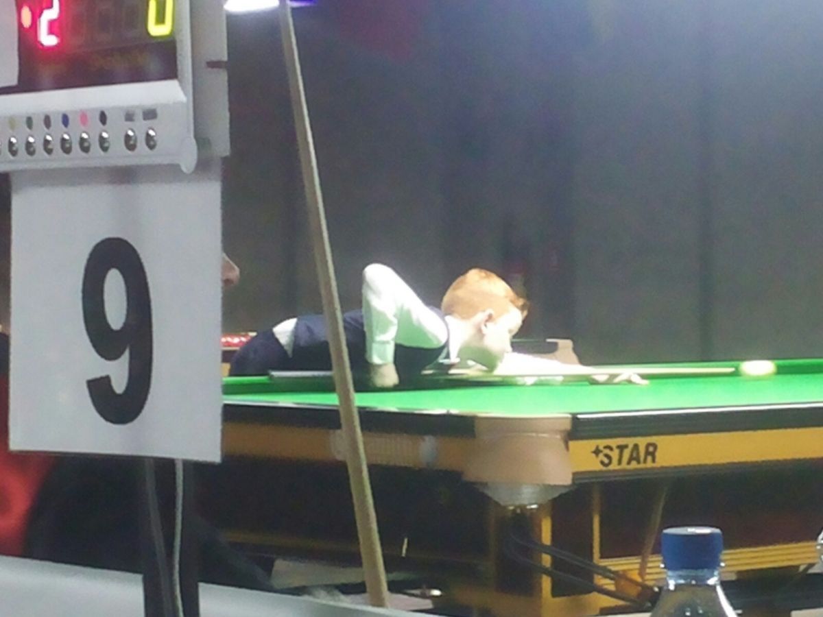 Snookerspeler, leunend op de tafel, klaar om een ​​bal te gooien. Scorebord zichtbaar.