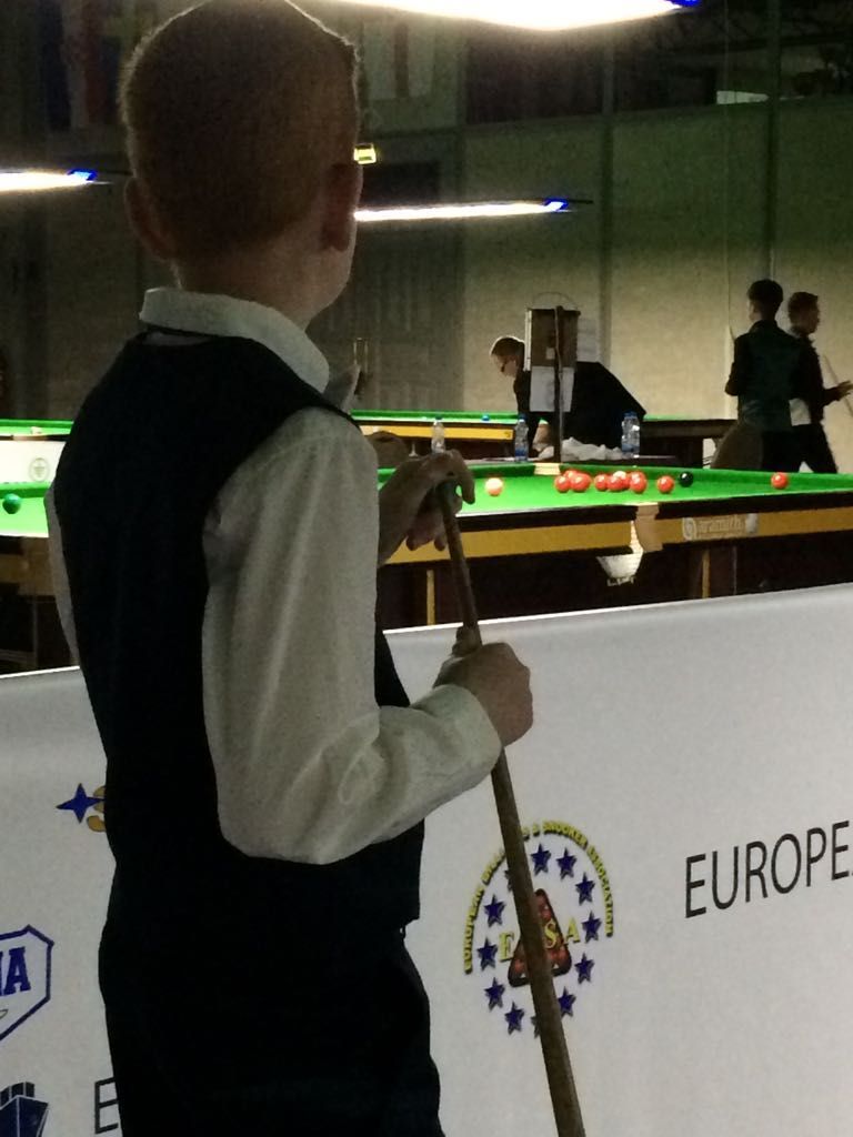 Een jonge jongen met een keu aan een snookertafel bekijkt het spel in een wedstrijdsituatie.