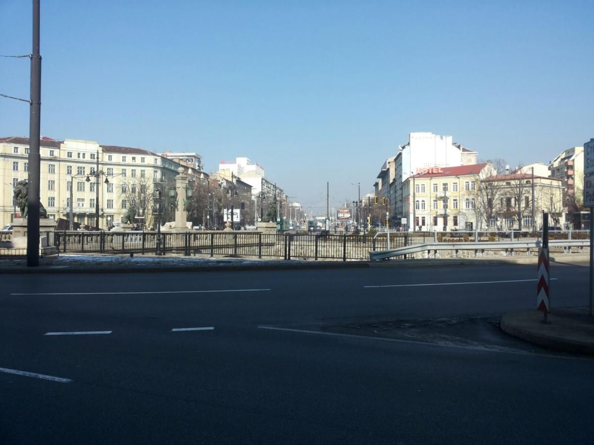 Straatbeeld met gebouwen langs een brede weg. Strakblauwe lucht erboven.