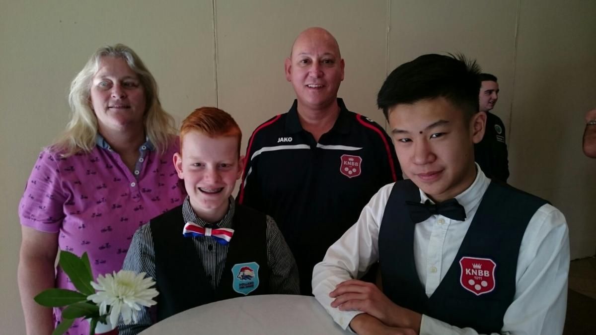 Gezin poseert voor een foto; een vrouw, een jongen met rood haar, een kale man en een tiener met een vlinderdas, binnen.