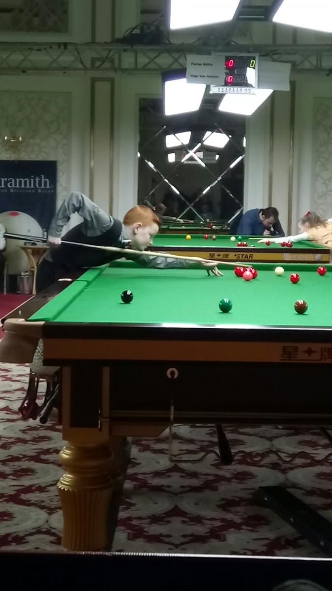 Een snookerspeler in actie, die een bal op een groene tafel probeert te slaan in een wedstrijdsituatie.