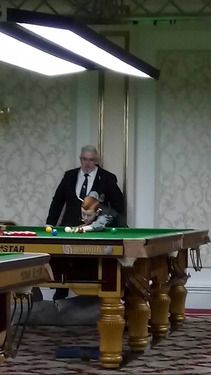 Man in pak speelt biljart, met een keu in de hand. Groene tafel, ballen en een rijkversierde kamer.