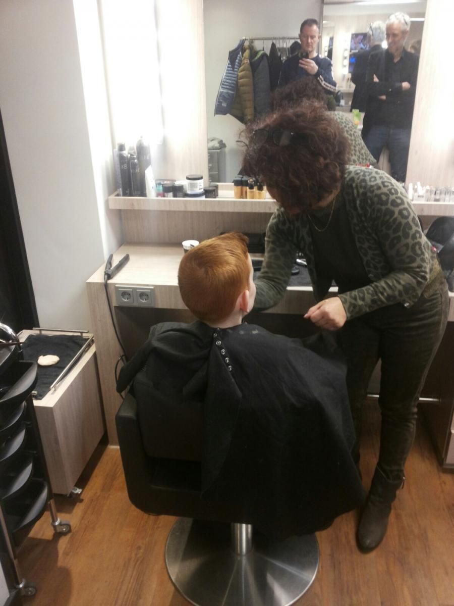 Een kapper knipt het haar van een jonge roodharige jongen in een salon. Mannen in de spiegel kijken toe.