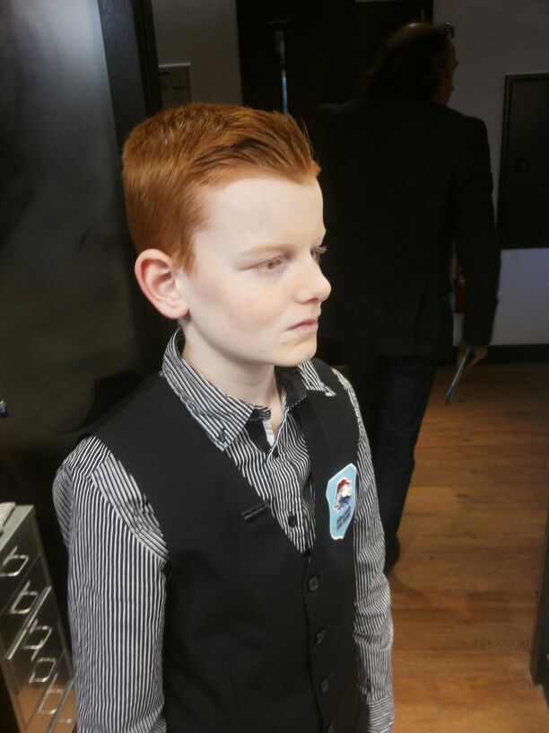 Jonge jongen met rood haar, gekleed in een vest en overhemd, kijkt opzij.