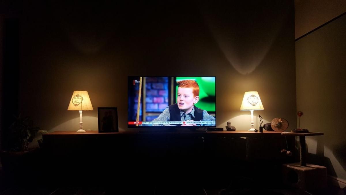 Een schemerige kamer met een televisie waarop een programma wordt uitgezonden, geflankeerd door twee lampen op een donkere tafel.