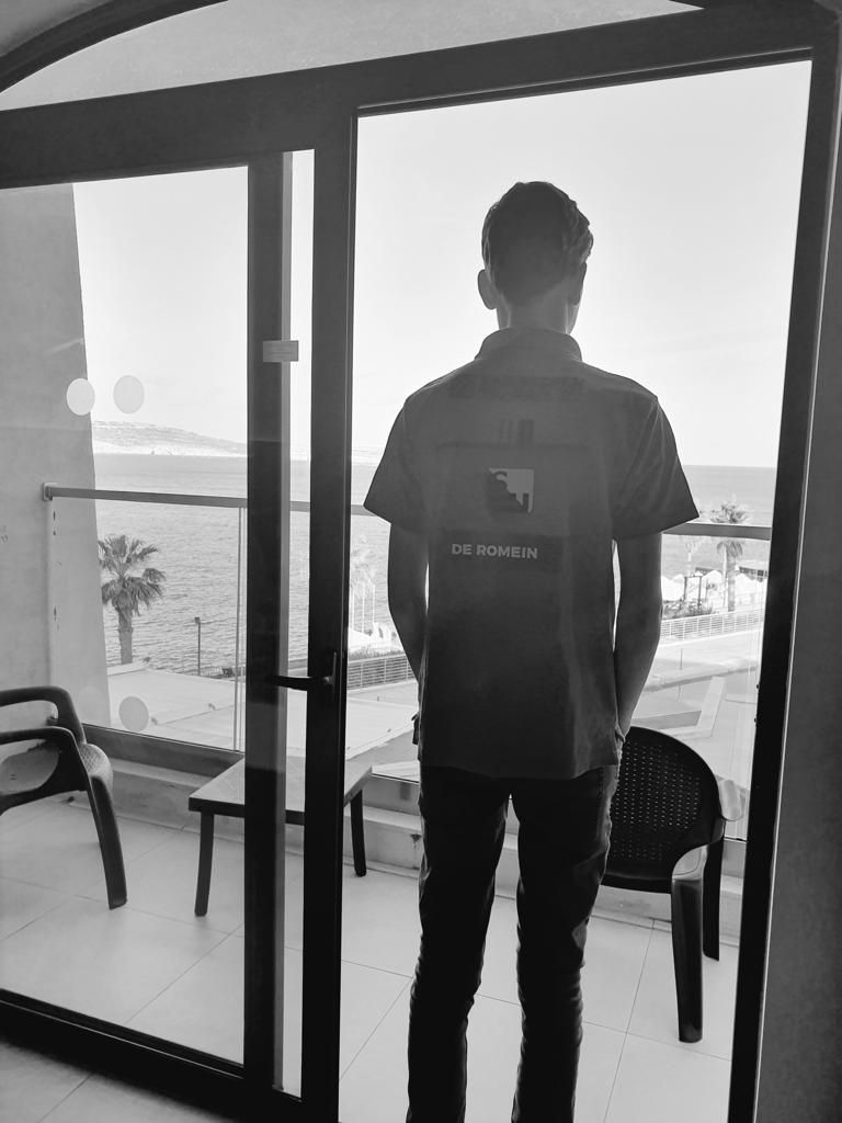 Persoon in uniform kijkt vanaf het balkon uit over de oceaan. Zwart-witfoto.