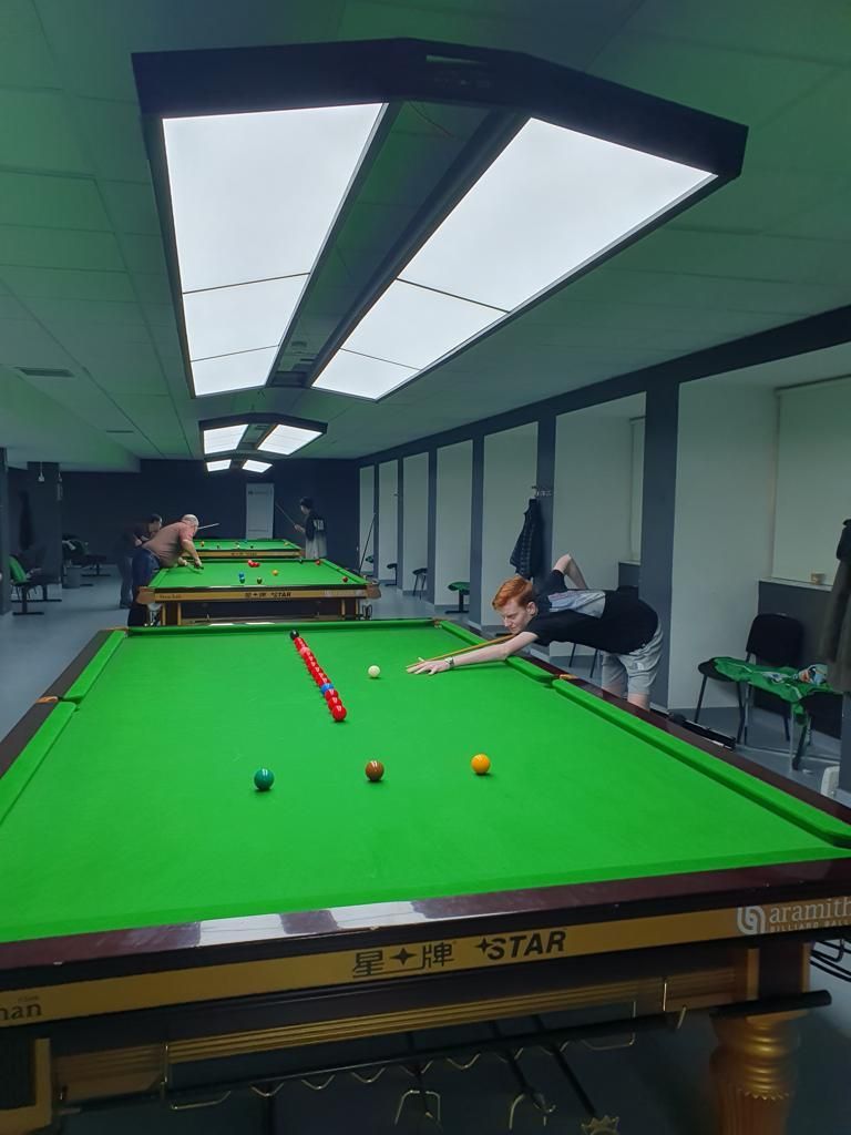 Snookerzaal met spelers die ballen schieten, ballen op de tafel, groen vilt, plafondverlichting.