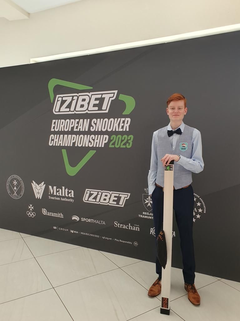 Jongeman in formele kleding met keu-koffer tijdens het Europees Kampioenschap Snooker 2023, tegen een achtergrond.