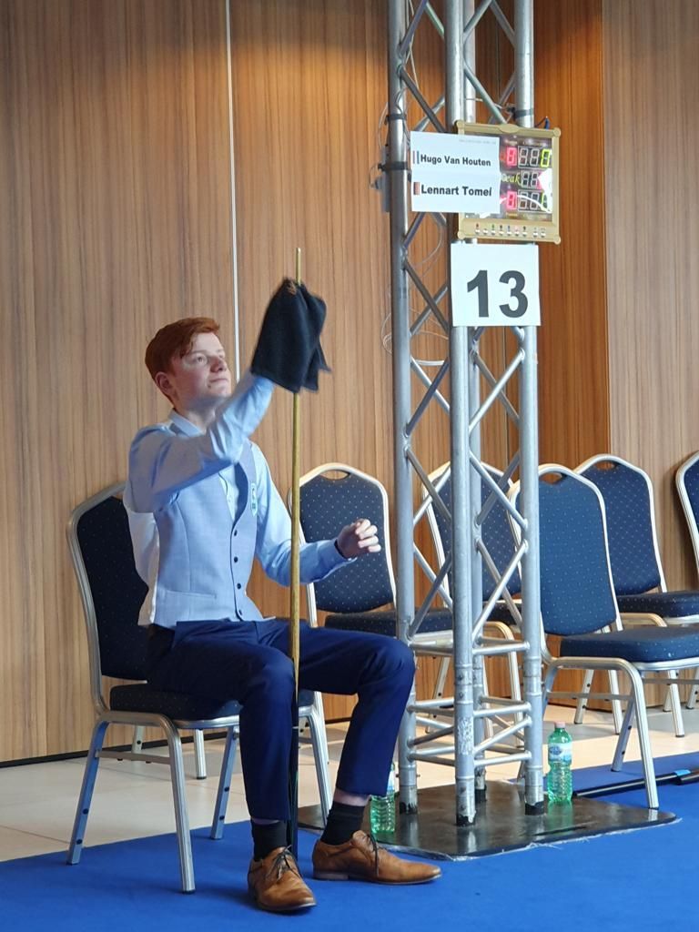 Jongeman in een blauwe outfit maakt een keu schoon, zittend bij een tafeltje met nummer 13.