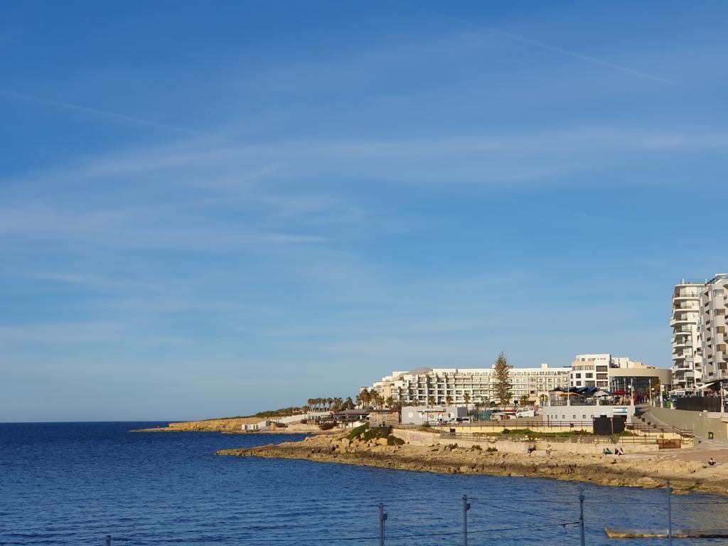 Kustlijn met gebouwen onder een strakblauwe lucht; links de zee.