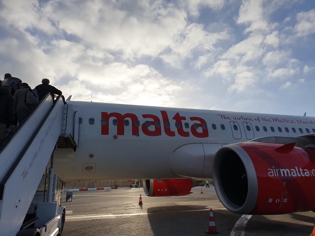 Mensen stappen op een zonnige dag aan boord van een Air Malta-vliegtuig.