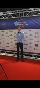 Een jongeman in pak poseert op de rode loper voor een kampioensbanner.