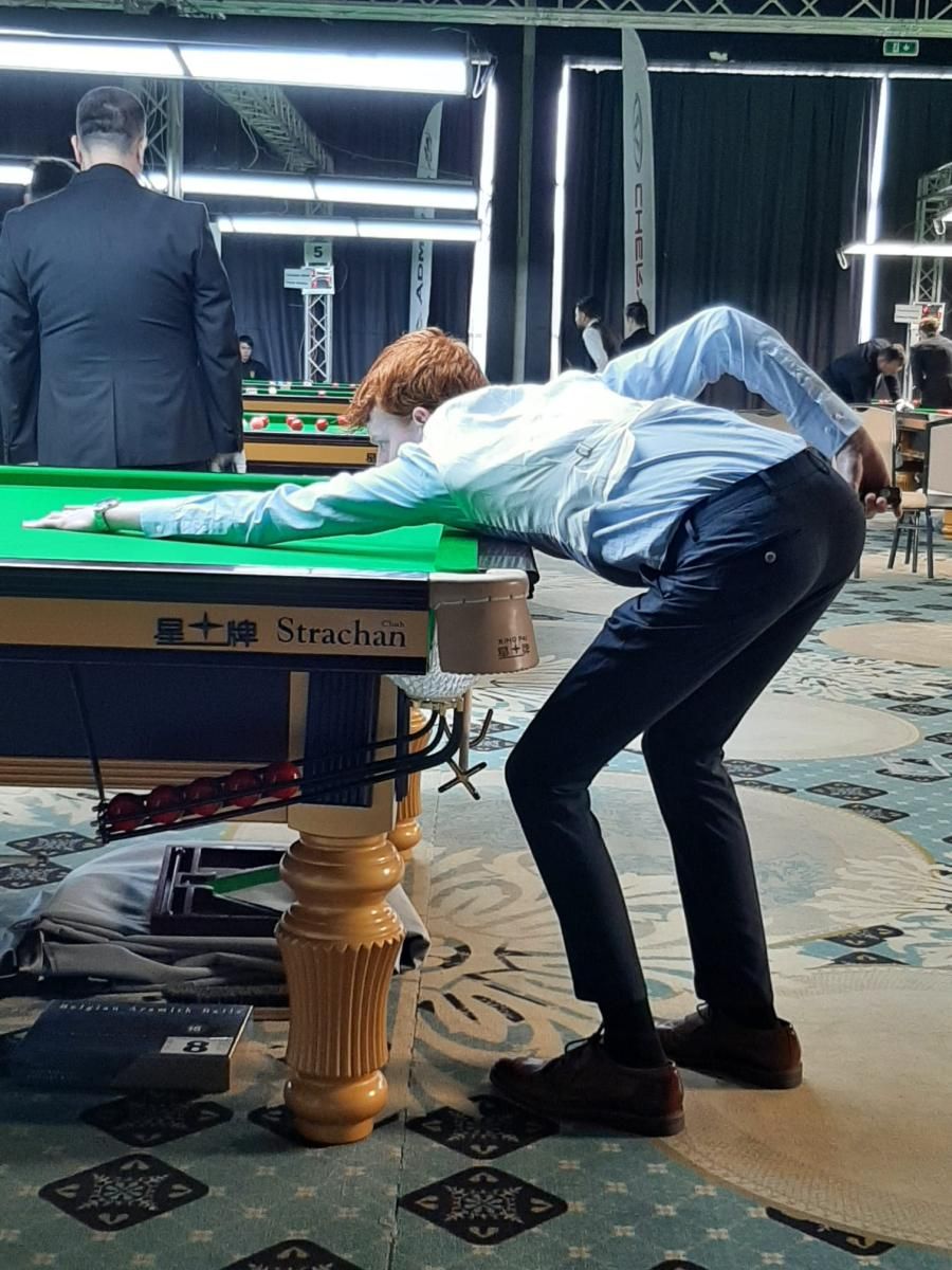 Een snookerspeler met rood haar buigt zich over een groene tafel en richt.