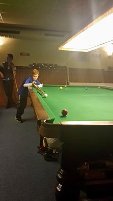 Een jonge jongen speelt snooker en mikt op de rode bal op een groene tafel in een snookerhal.