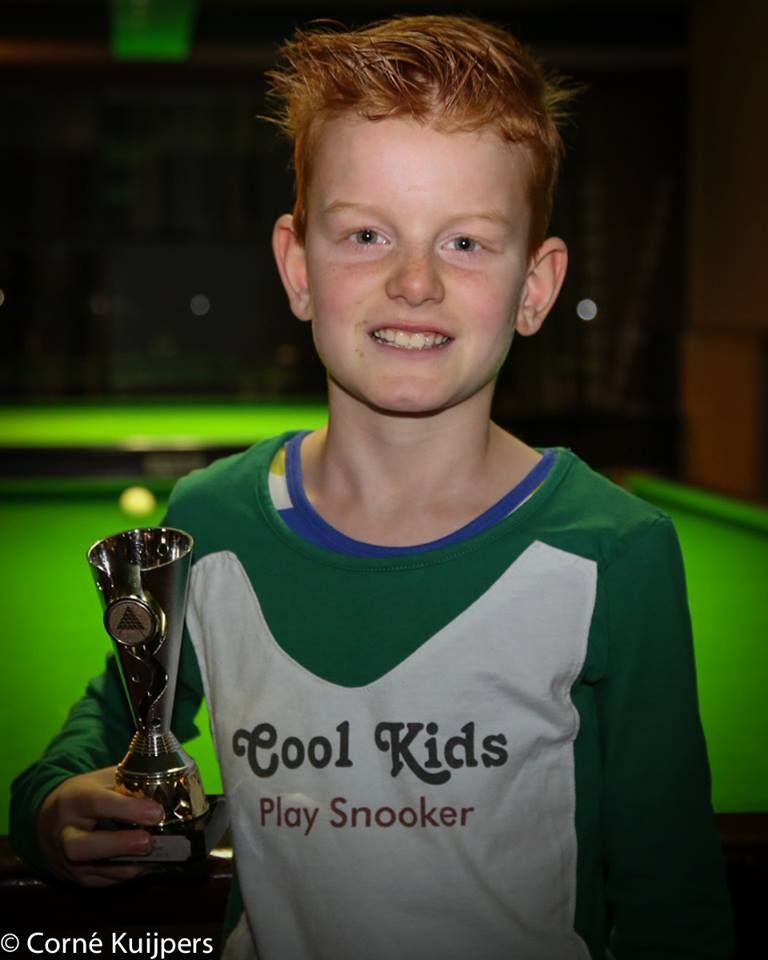 Jonge jongen met rood haar houdt een trofee vast en draagt ​​een groen shirt met de tekst 