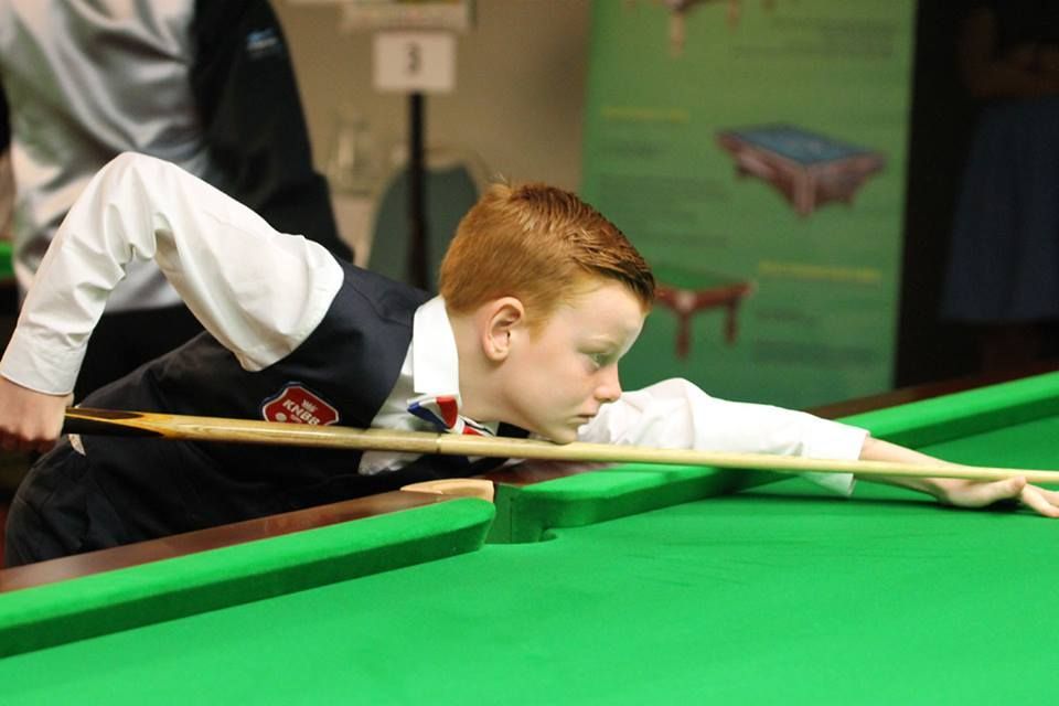 Een jongen in formele kleding bereidt een bal voor op een groene pooltafel.