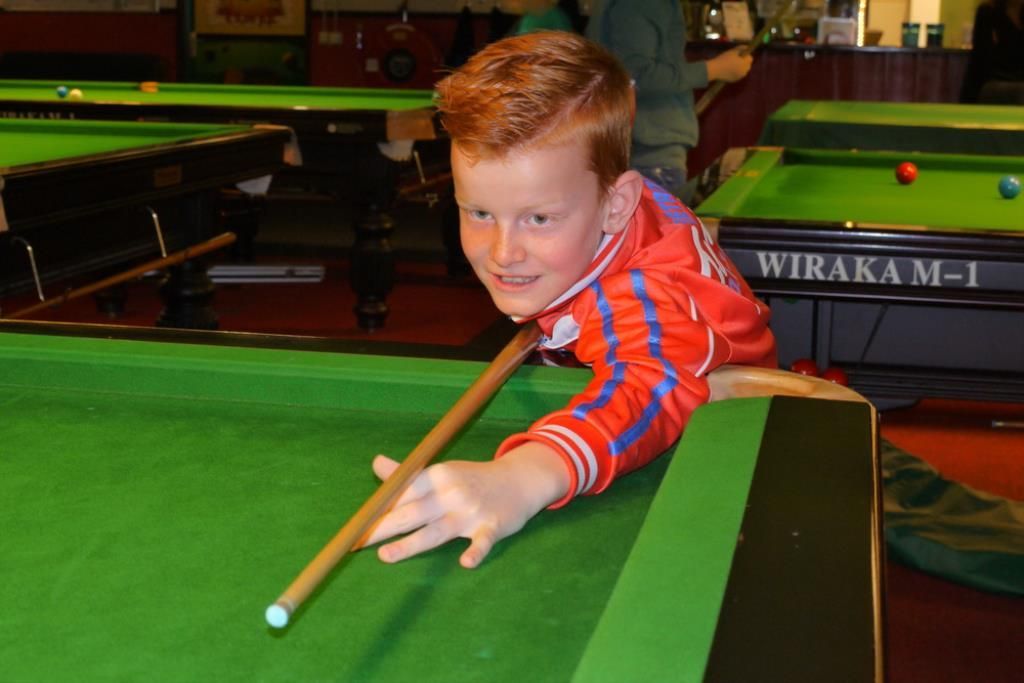 Jonge roodharige speelt pool, lacht, draagt ​​een rood-blauw gestreept shirt en richt haar keu op een bal.