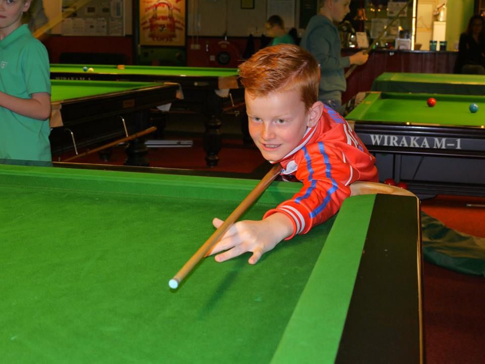Een jonge jongen met rood haar speelt biljart en richt op een bal op de groene tafel.