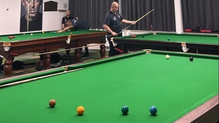 Man met keu staat op het punt om een ​​potje te spelen in een snookerhal, gefocust op de gekleurde ballen op de tafel.