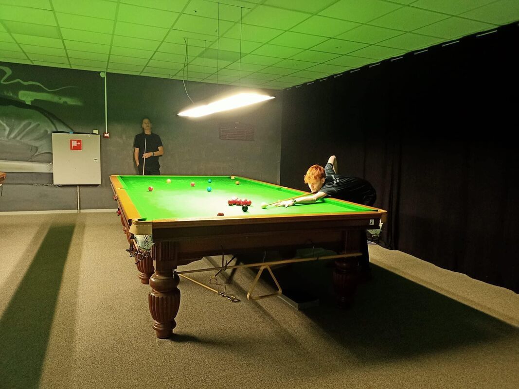 Een snookerspeler bereidt zijn bal voor op een groene tafel in een slecht verlichte kamer.