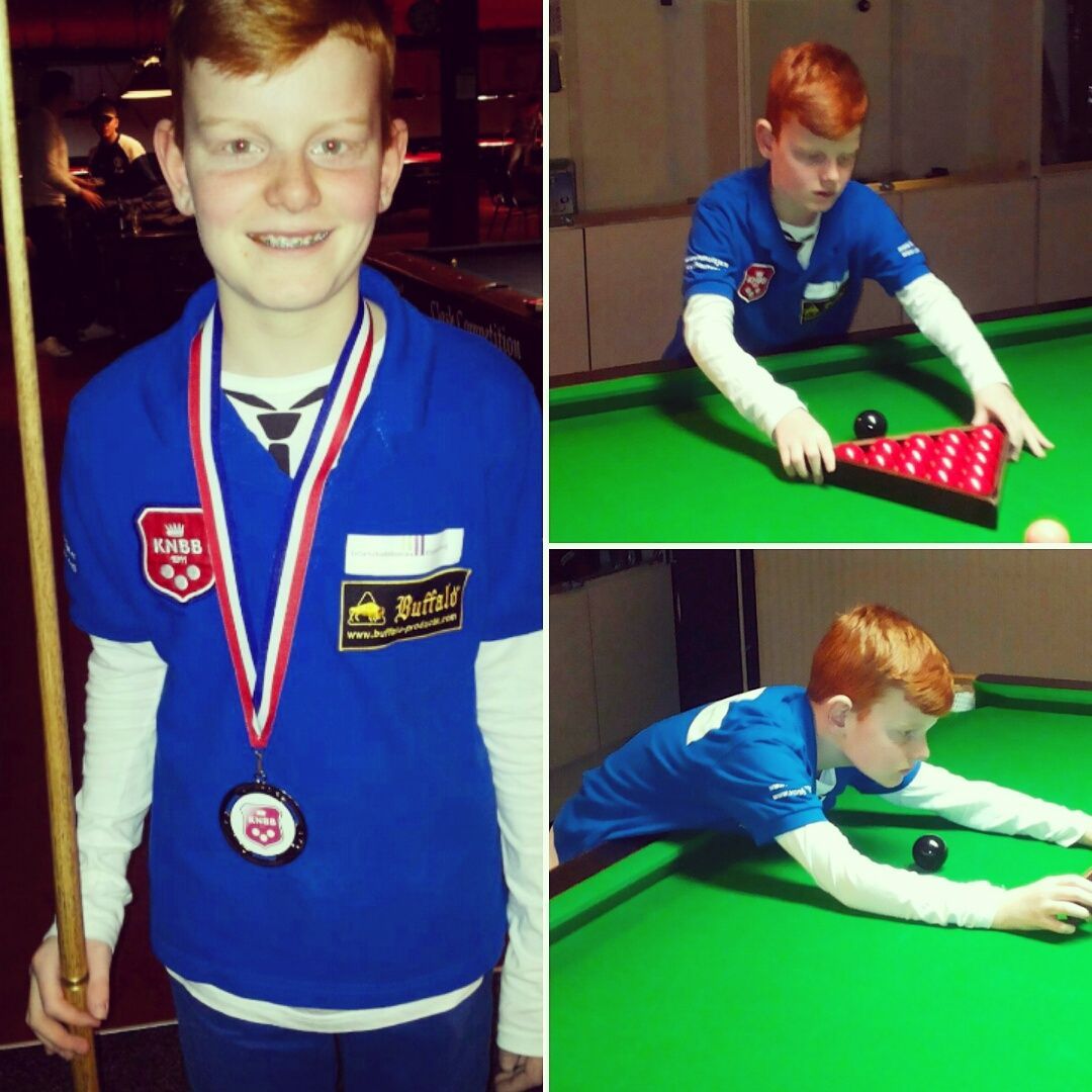 Jonge roodharige snookerspeler in een blauw shirt en met een medaille oefent op een groene tafel.