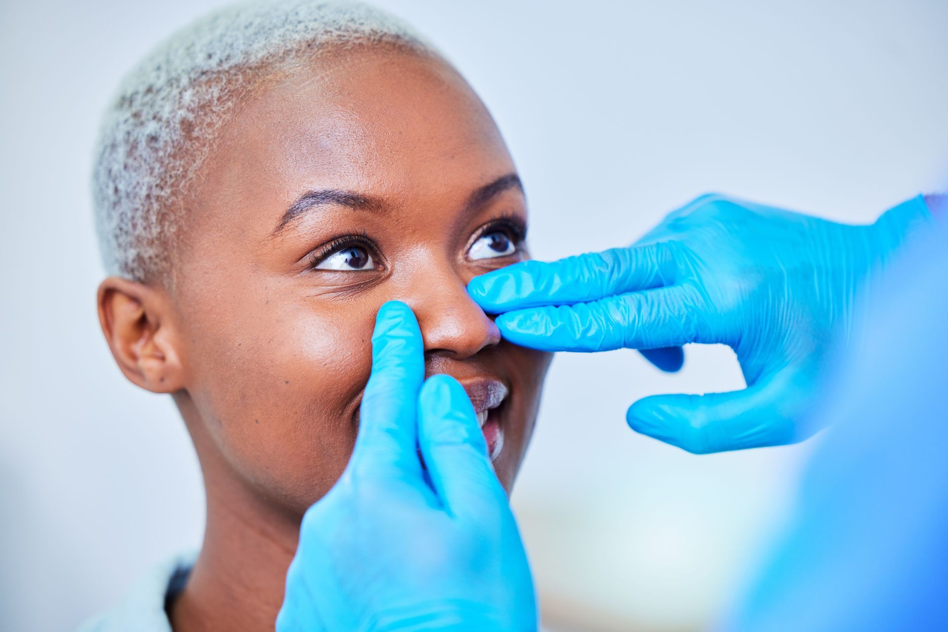 A person's nose being examined by someone wearing blue gloves; indoors.