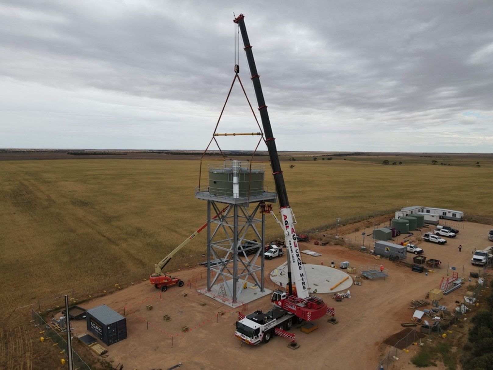 An aerial view of a crane lifting a water tower in a field.