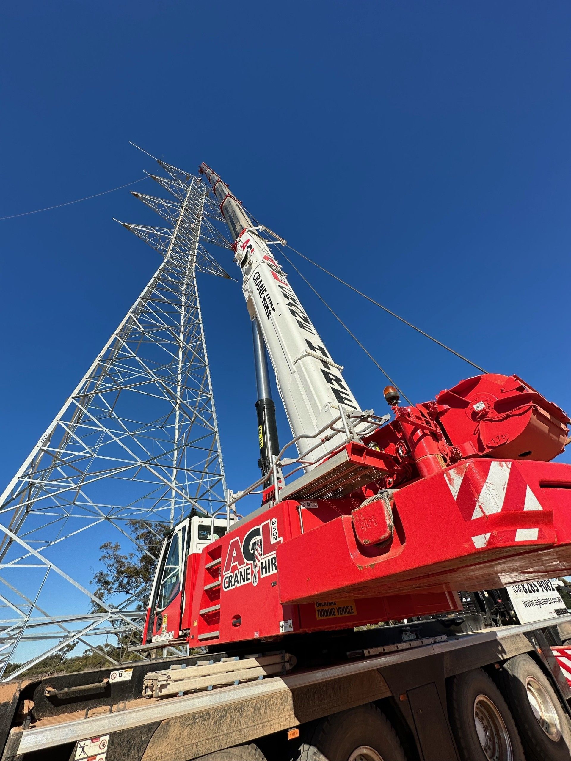 Red crane lifting an electrical power tower against a blue sky.