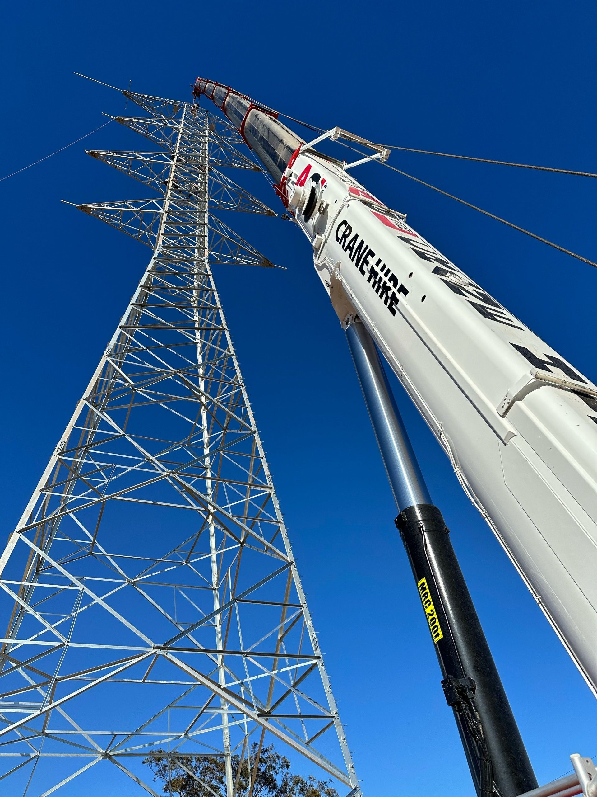 Crane working on an electricity pylon against a clear blue sky.
