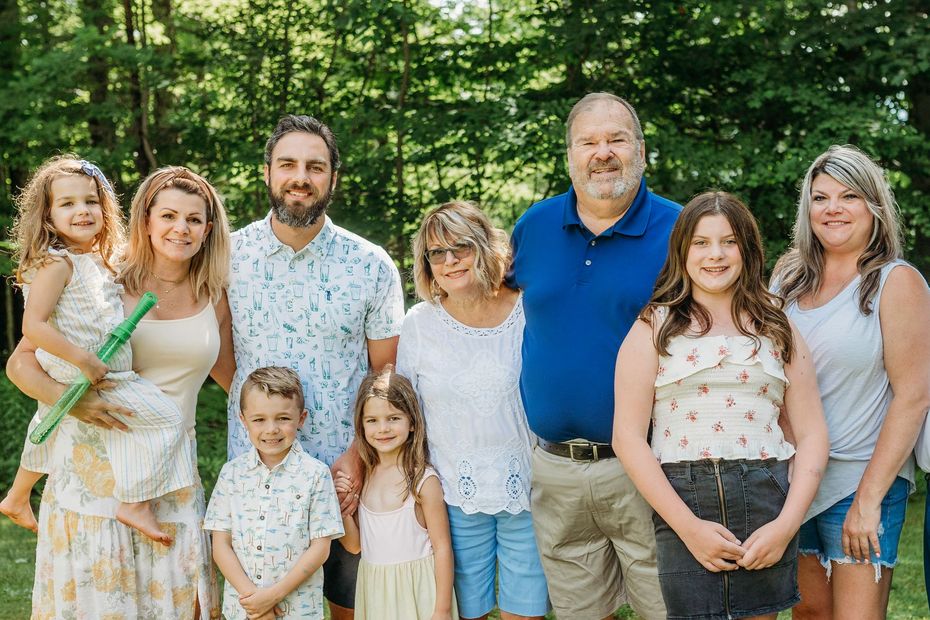 A large family is posing for a picture together in front of trees.