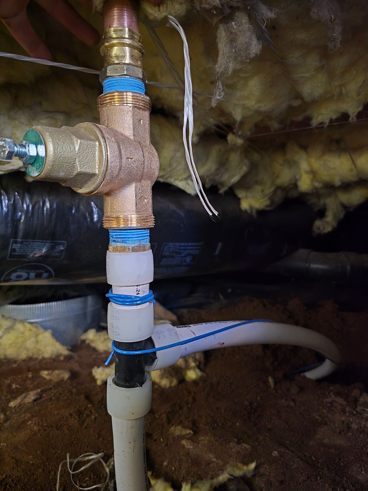 Copper plumbing valve connected to white plastic piping in a crawlspace with insulation.