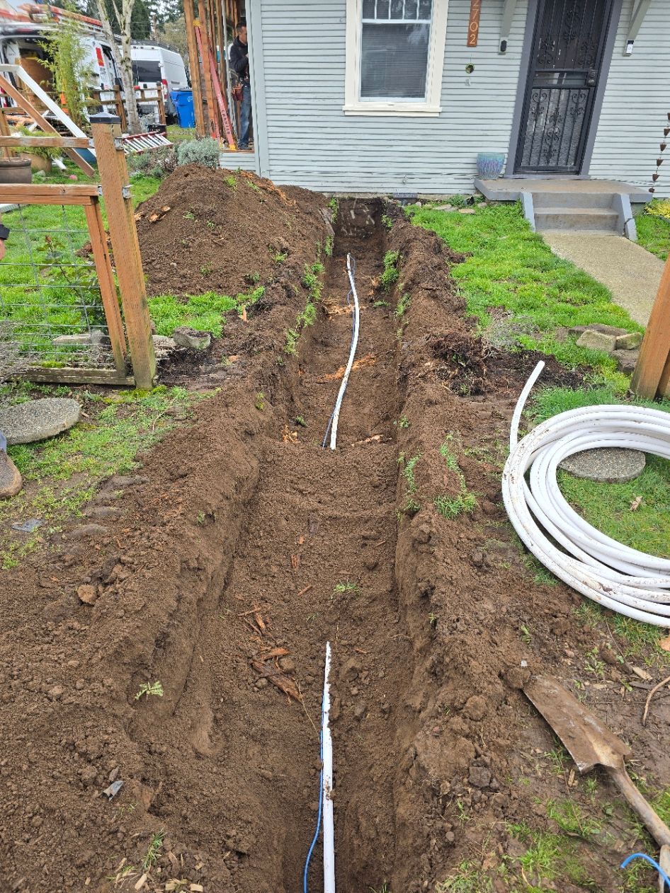 Trenched dirt yard leading to a house, with a white pipe running along the ground.