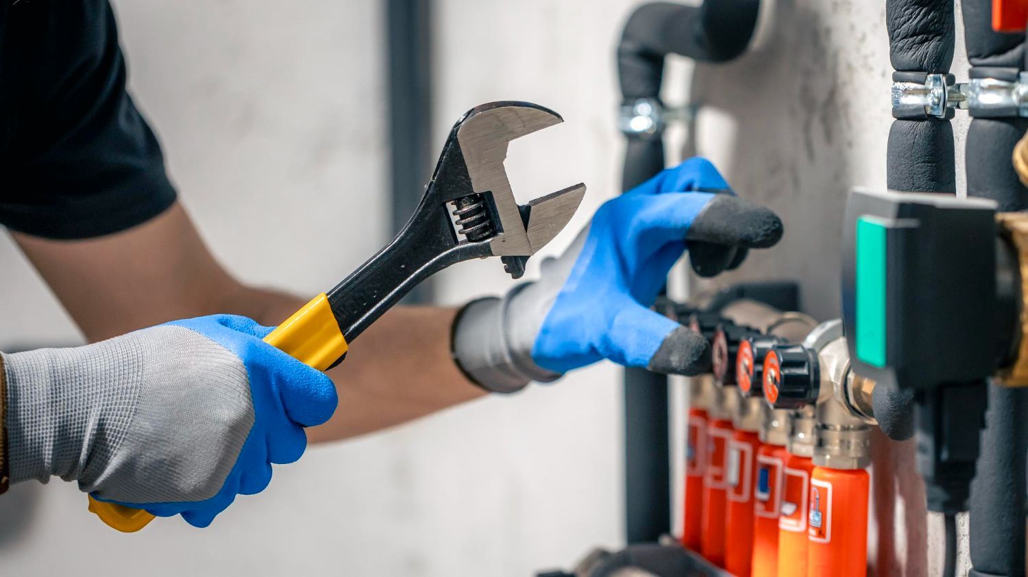 Gloved hands using a wrench to adjust a pipe valve in an industrial setting
