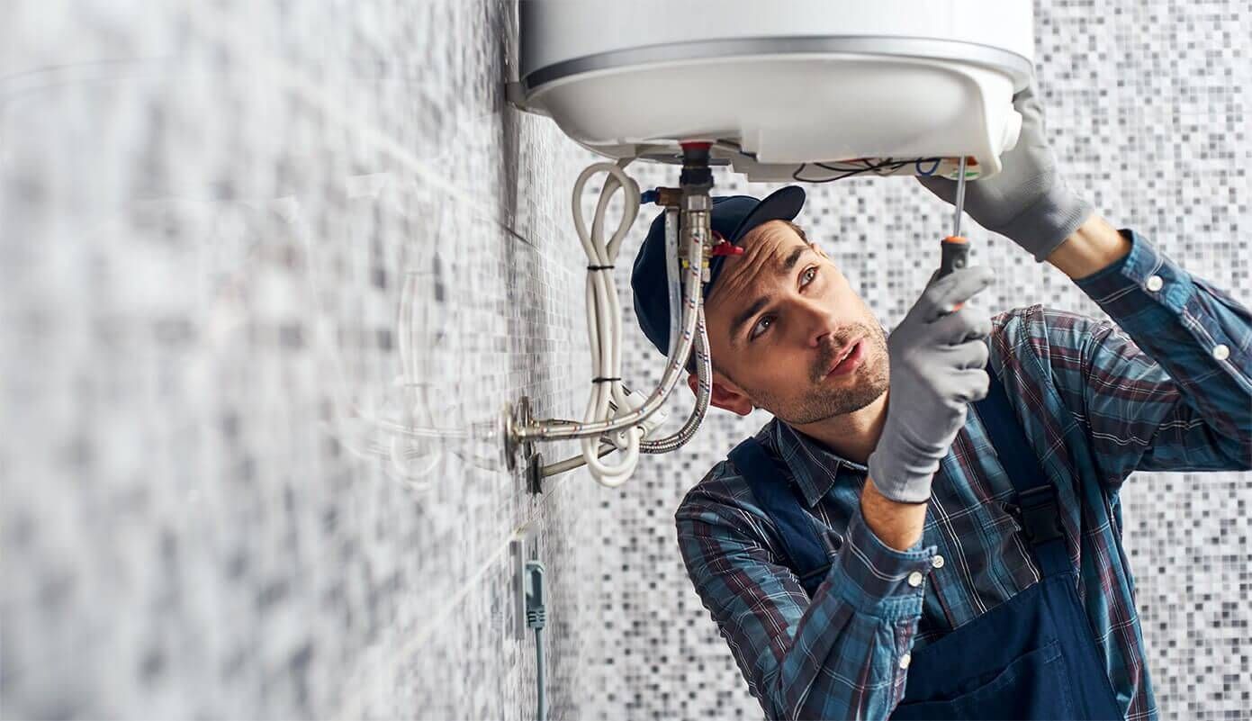 Technician adjusting a wall-mounted water heater with tools in a tiled room