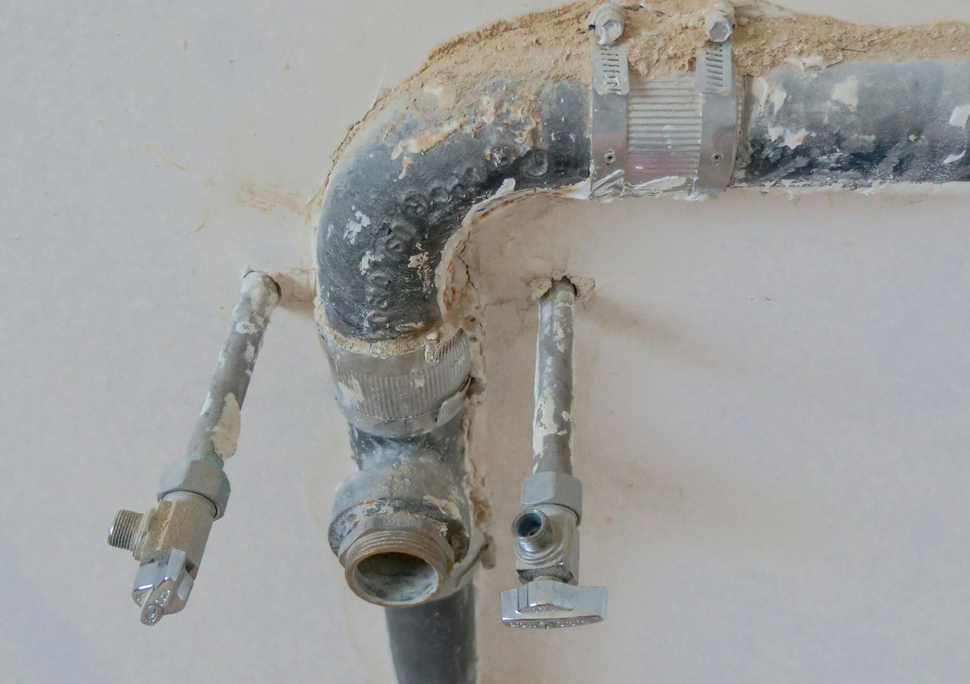 Close-up of rusty metal plumbing pipes and fittings against a light wall.