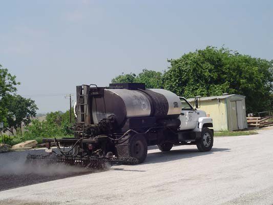 A tanker truck is spraying asphalt on a road