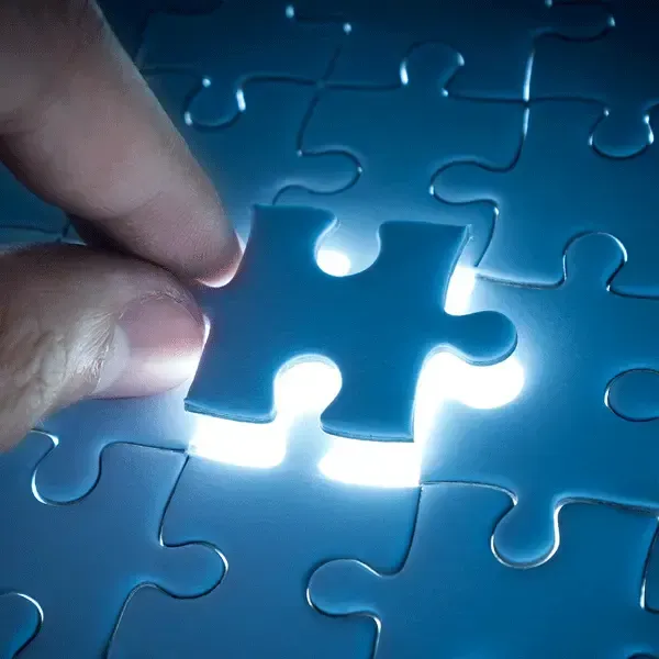 Hand holding a puzzle piece over a glowing puzzle space