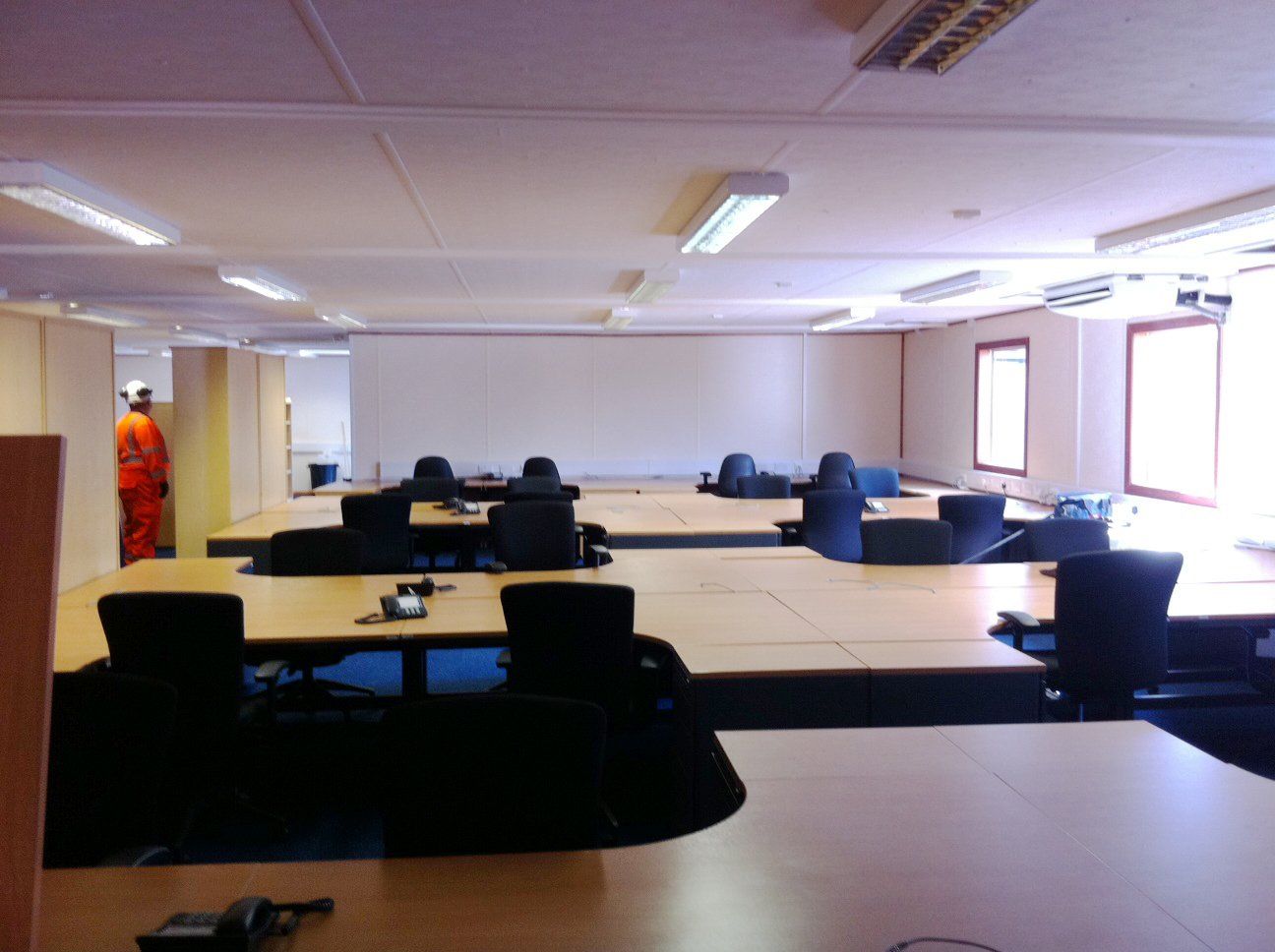 A spacious, empty office room featuring multiple desks and chairs arranged neatly