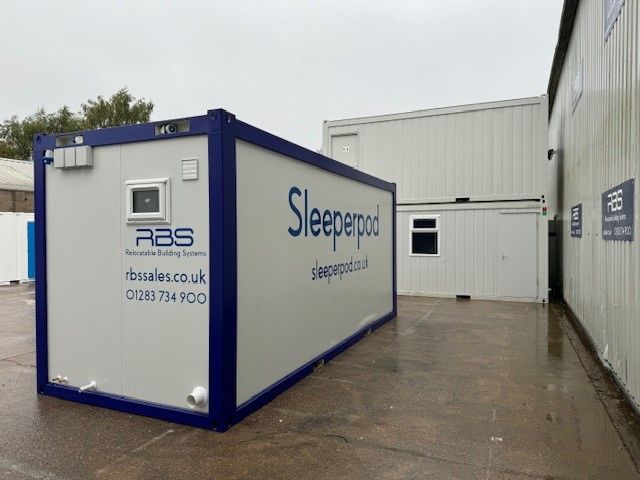 A blue and white sleeper pod is sitting outside of a building
