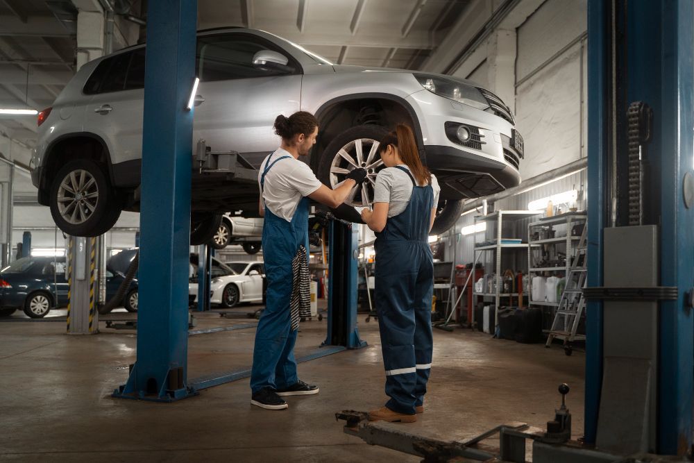 Two women are working on a car in a garage.