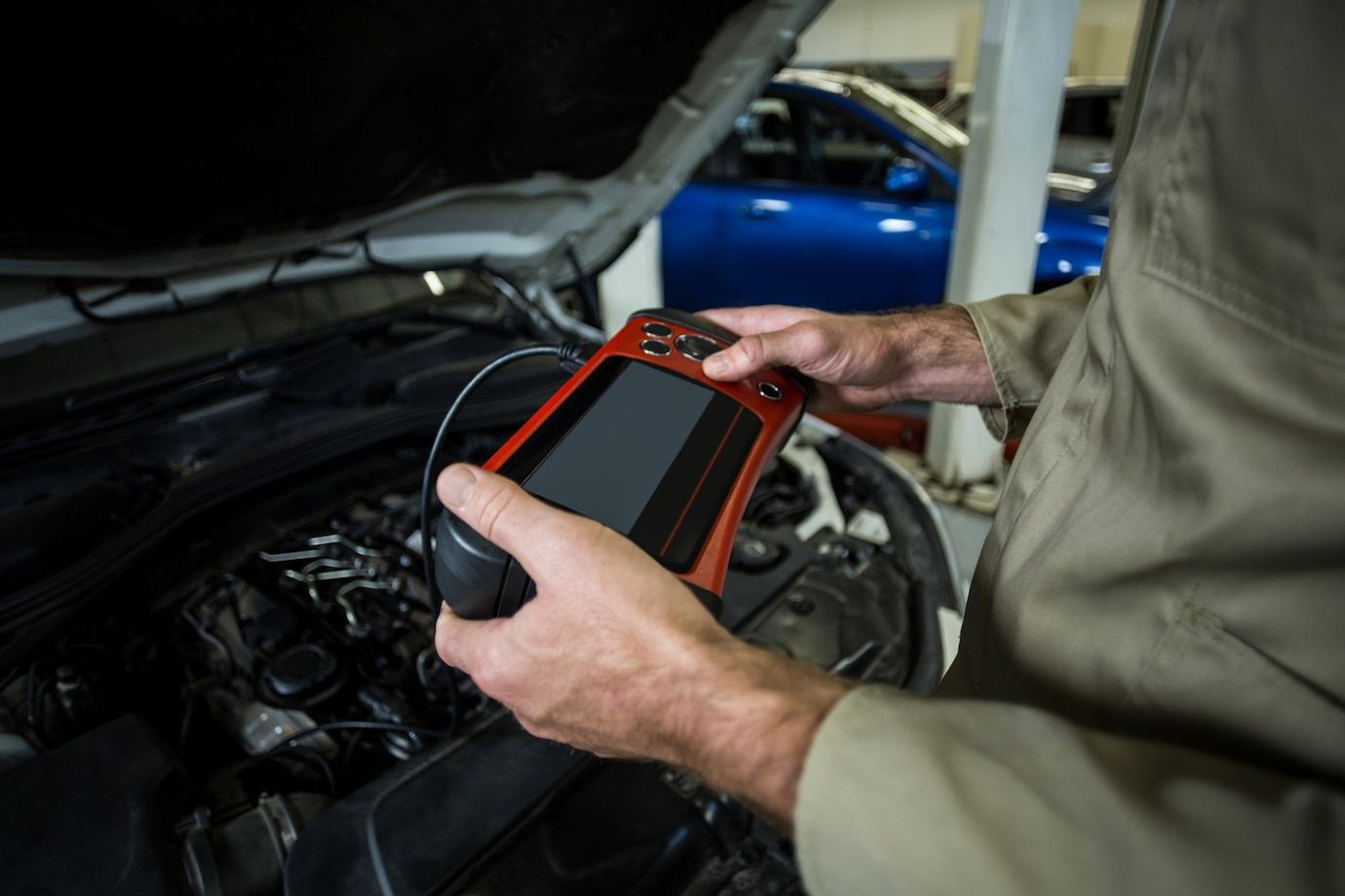 A man is holding a device in front of a car engine.