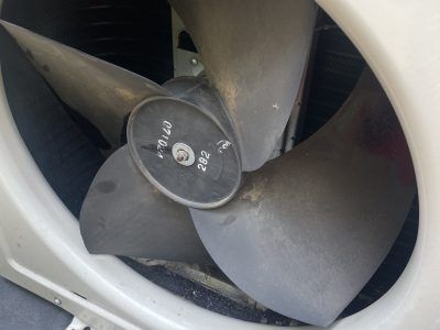 Close-up of a dusty air conditioner fan with four blades inside a white housing.