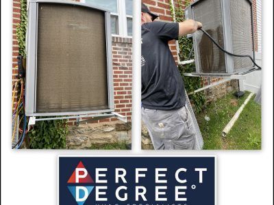 Man power washing a dirty AC unit outside a brick building.