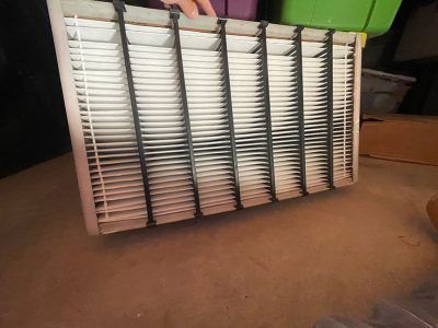 Dirty air filter with black streaks, held by hand. Beige frame, white pleated filter material.