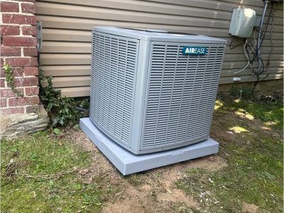 Gray AirEase air conditioning unit on a concrete pad next to a brick wall and siding.