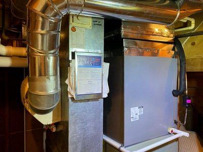 Furnace and ductwork in a basement. Metal components are silver, with white pipes and a gray unit.