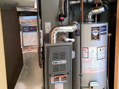 Furnace, water heater, and air filter in a utility closet. Metal ductwork and pipes are visible.