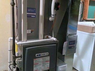 An AirEase furnace in a basement setting. The unit is gray and white, with connected pipes and ducts.